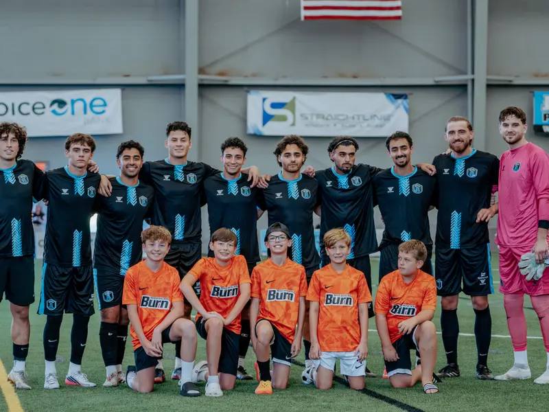 Detroit Metro FC players pose with youth players in orange kits before a match